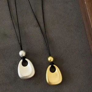 Vue détaillée des colliers à pendentif en métal mat doré et argenté avec cordons noirs.