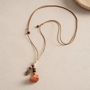 Détail d'un collier ethnique avec rose en céramique et feuille en métal sur cordon.