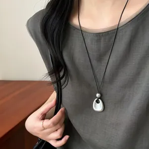Gros plan d'un collier avec pendentif géométrique en argent mat sur cordon noir long