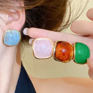 Close-up of square resin stud earrings in blue, pink, amber, and green color options.