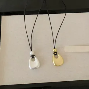 Vue détaillée des pendentifs dorés et argentés mats sur des colliers minimalistes noirs.