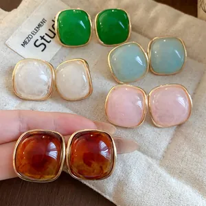 Detailed macro shot of various colored square resin stud earrings on a minimalist beige pouch