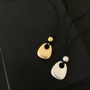 Vue détaillée de colliers pendentifs minimalistes en métal mat or et argent sur fond noir