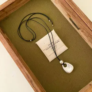 Vue détaillée d'un collier avec pendentif en argent mat et perle blanche sur cordon noir