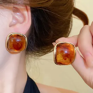 Detail shot of vintage amber resin square stud earrings with gold frame and silver needles.