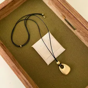 Vue détaillée d'un collier pendentif en or mat sur un plateau en tissu vert élégant