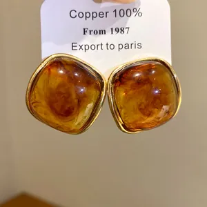 Detail view of square amber resin stud earrings with textured gold-tone metal frame.