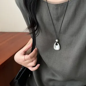 Vue détaillée d'un collier avec pendentif en métal argenté mat et cordon noir.