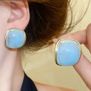 Close-up of light blue resin square stud earrings with elegant gold-tone metal borders