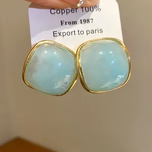 Close-up of light blue resin square stud earrings with elegant gold metal frame detail