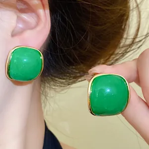 Close-up of vibrant green resin square stud earrings with gold trim shown worn on ear