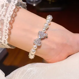Nahaufnahme eines eleganten Perlenarmbands mit Zirkonia-Schleifen-Detail am Handgelenk.