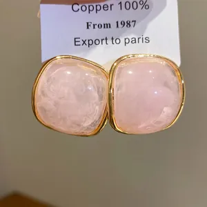 Detailed macro view of pink resin square stud earrings with textured gold copper frames