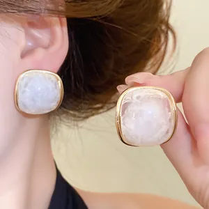 Close-up of elegant square resin stud earrings with white marble pattern and gold trim