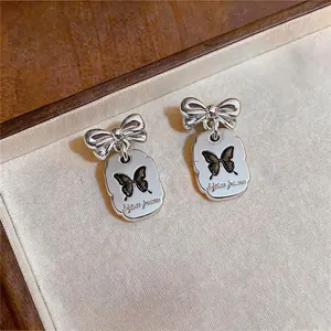 Elegantes pendientes de lazo plateado con dijes de mariposa en un joyero de lujo