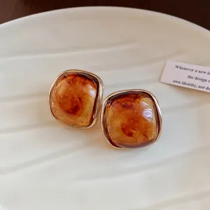 Detailed macro view of amber resin square stud earrings with elegant gold borders.