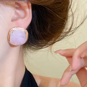 Macro detail of a pink square resin stud earring with gold-toned border worn by a model