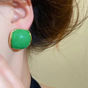 Close-up of green resin square stud earrings with gold border on model's ear
