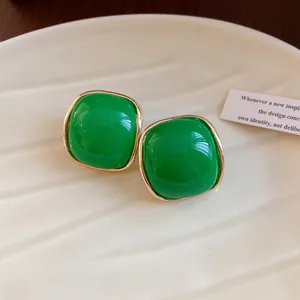 Close-up view of vintage green square resin stud earrings with gold borders on a cream plate