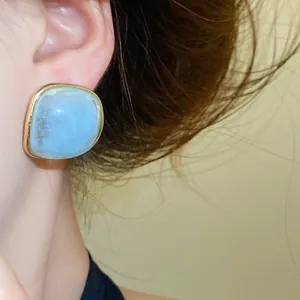 Detailed close-up of a light blue marble texture resin earring with gold metal border