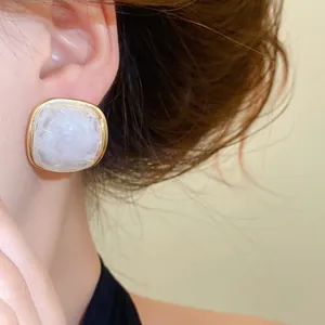 Close-up of elegant square resin stud earrings with gold border and white marble texture