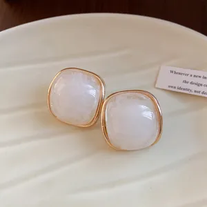 Detailed macro view of square white resin stud earrings with gold-toned border