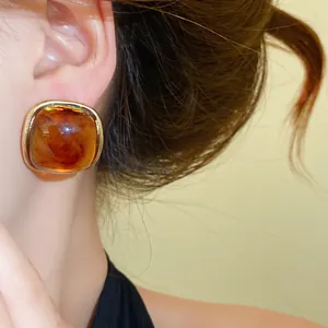 Close-up of amber resin stud earring with gold frame on model ear