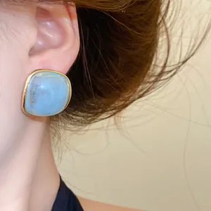 Close-up of sky blue resin stud earring with gold-tone border worn on ear