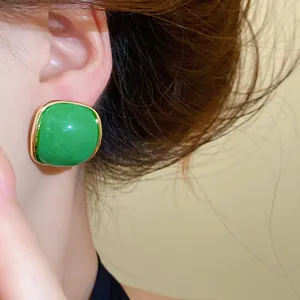 Detailed shot of green resin square stud earrings with elegant gold-tone border on ear