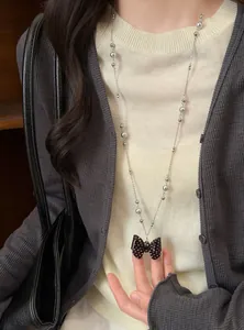 Detail van een lange ketting met een zwarte polkadots strikhanger en grijze parels