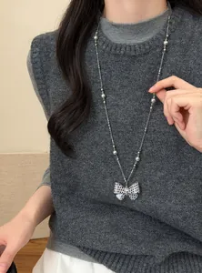 Detail van een ketting met een strikhanger met stippen gedragen op een grijs vest