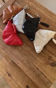 Kleurrijke mini lederen portemonnees in croissantvorm op een rustieke houten tafel.
