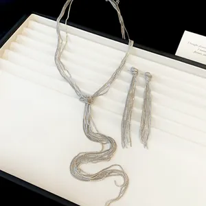 Gros plan sur un ensemble collier et boucles d'oreilles argentés avec pampilles et nœuds