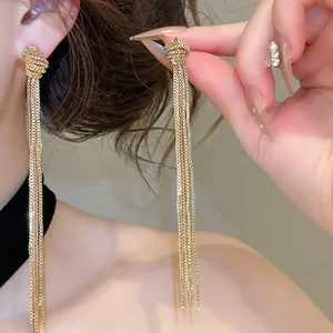 Gros plan de boucles d'oreilles dorées avec design à nœud et longues franges en chaîne