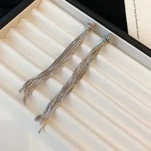 Détail de boucles d'oreilles minimalistes à pompons en argent avec chaîne nouée.