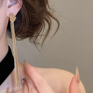Gros plan de boucles d'oreilles à pompons en chaîne dorée nouée sur un mannequin.
