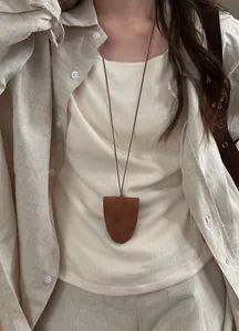 Close-up of brown suede magnetic pendant necklace for holding glasses on beige linen outfit.