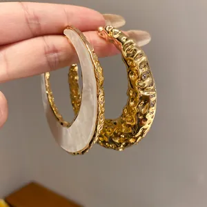 Detailansicht goldene C-förmige Ohrringe mit weißem Acetate-Inlay.