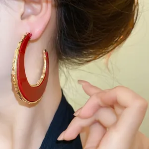 Detailansicht eleganter C-förmiger Creolen in Rot und Gold am Ohr für einen glamourösen Look.