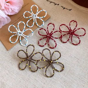 Group of three pairs of polka dot painted hollow flower stud earrings on beige linen