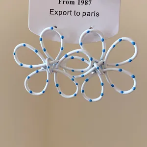 Macro view of white flower drop earrings with blue polka dots and painted finish