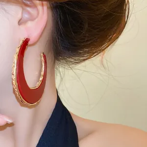 Detailansicht eines großen rot-goldenen Ohrrings in C-Mondform an einem Frauenohr