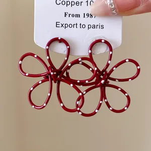 Detail of red hollow flower earrings with white polka dots and silver needle posts.