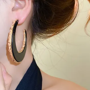 Nahaufnahme des übergroßen schwarzen und goldenen C-förmigen Halbmondohrrings am Model