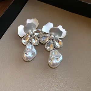 Close-up detail view of elegant silver flower drop earrings with rhinestones and baroque pearls.
