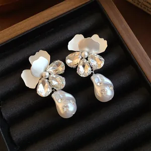Close-up detail of elegant white flower earrings with crystals and baroque pearl drops