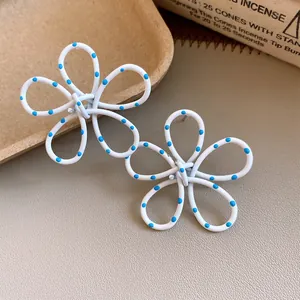 Detailed view of matte white hollow flower stud earrings decorated with blue polka dots
