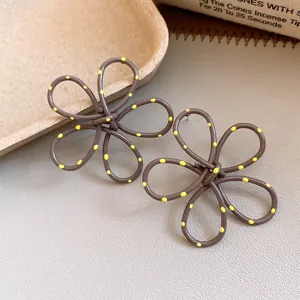 Close-up of brown spray-painted flower earrings with yellow polka dots and hollow design.