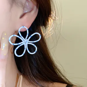 Macro view of white flower stud earrings with blue polka dots shown being worn on ear