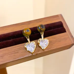 Macro view of heart zircon earrings with tiger's eye beads on wooden stand.